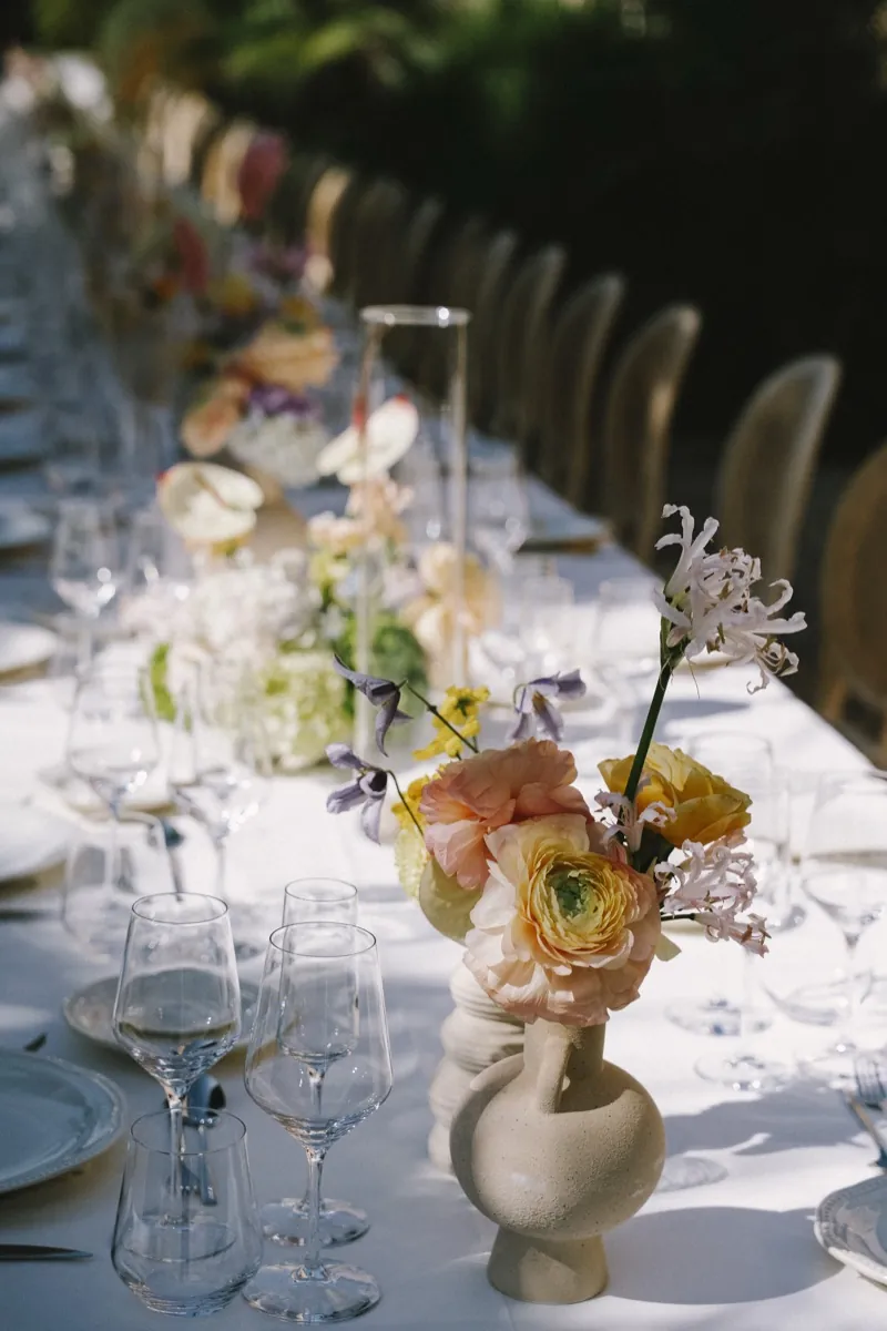 A long banquet table laid for dinner, pastel flowers in a ceramic vase, shot on 35mm film, Biniagual, Mallorca