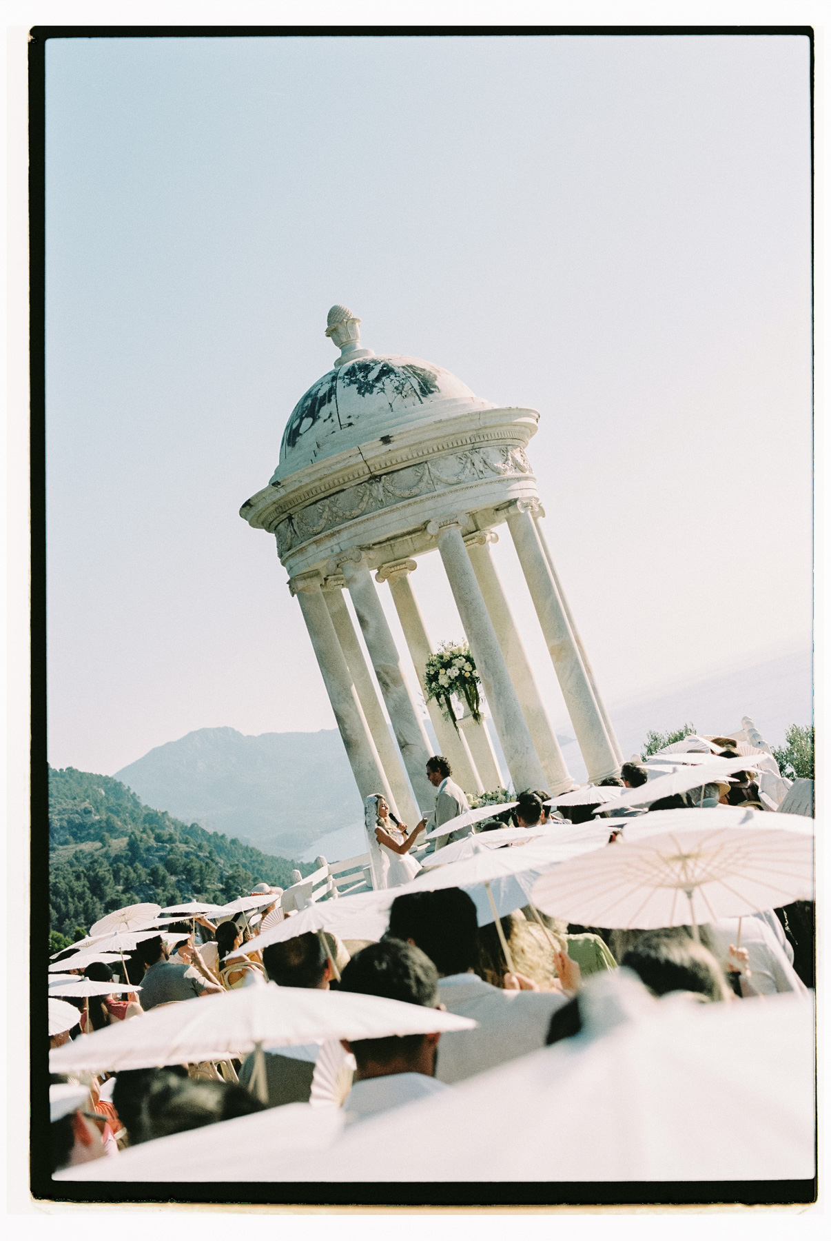 The marble rotunda above the valley, guests and white parasols below, shot on 35mm film in Mallorca