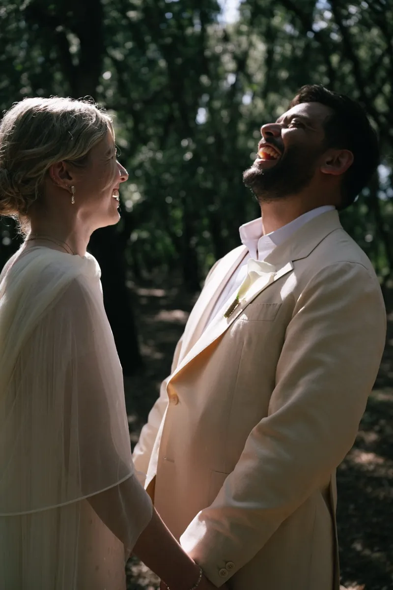 The couple hand in hand under the trees, the groom laughing, Finca Binissatí, Mallorca