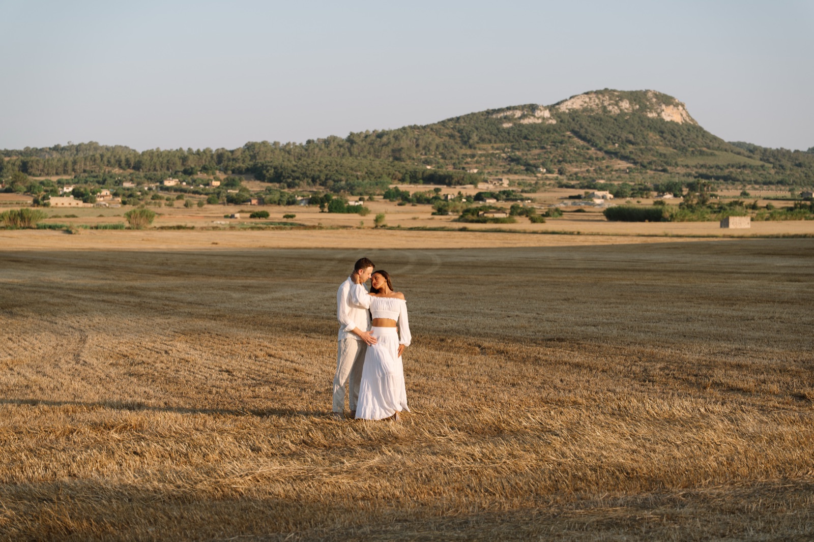 Irene and Daniel holding each other in a golden stubble field below the hills at Sineu, Mallorca