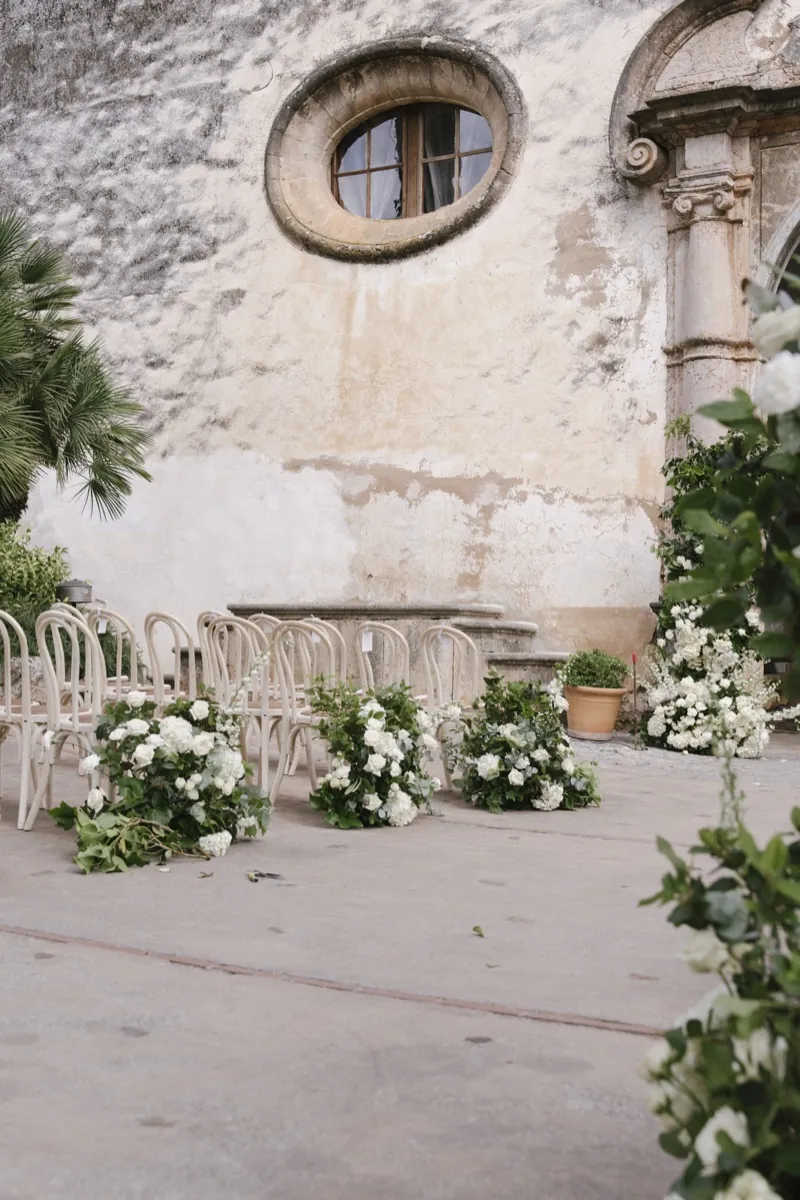 Ceremony chairs and white flowers set before the stone façade, Jardines de Alfabia, Mallorca