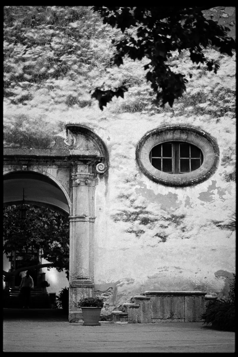 The arched stone façade and its round window seen from under the trees, Jardines de Alfabia, Mallorca