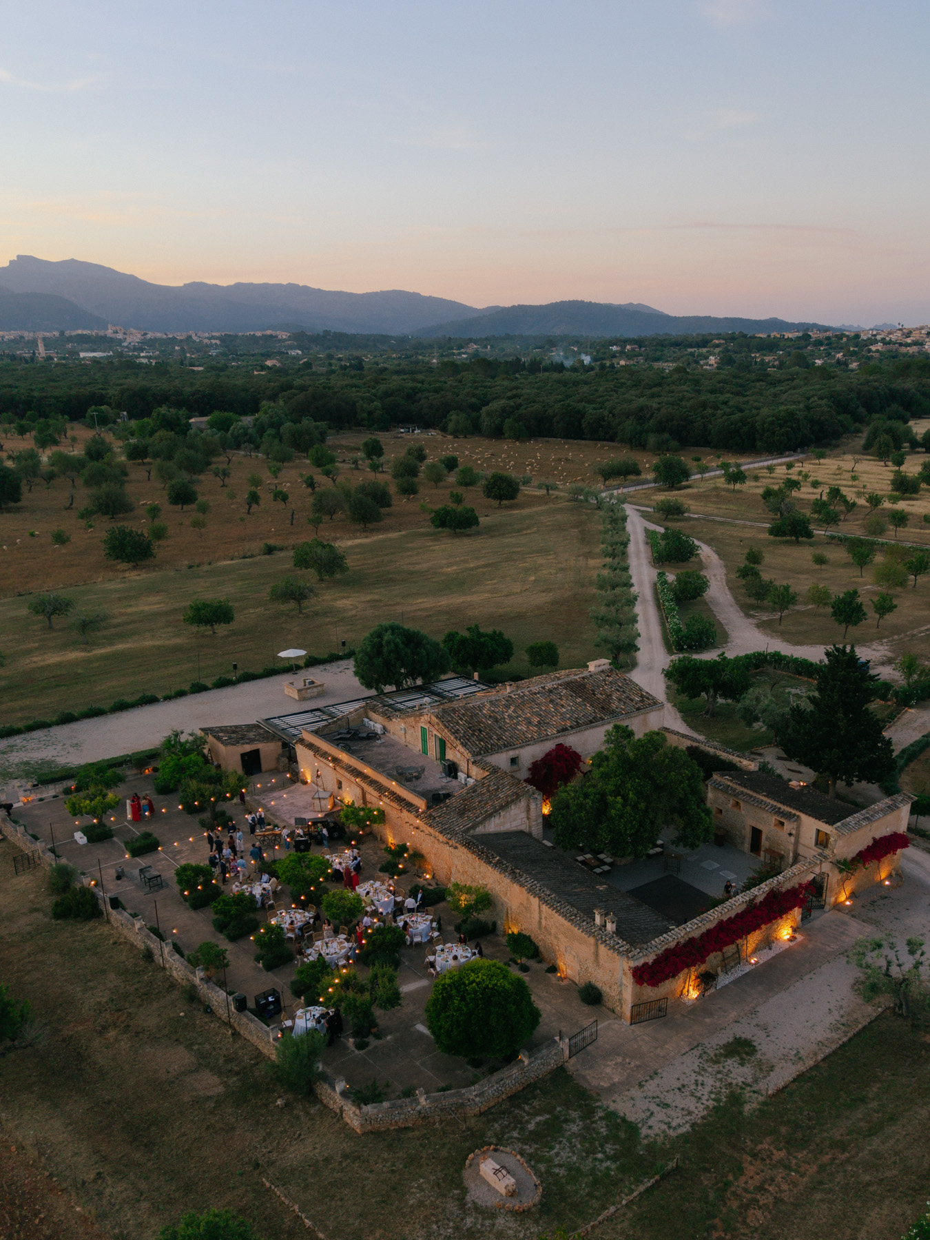 Finca Binissatí from the air at dusk, dinner tables lit in the courtyard, Mallorca